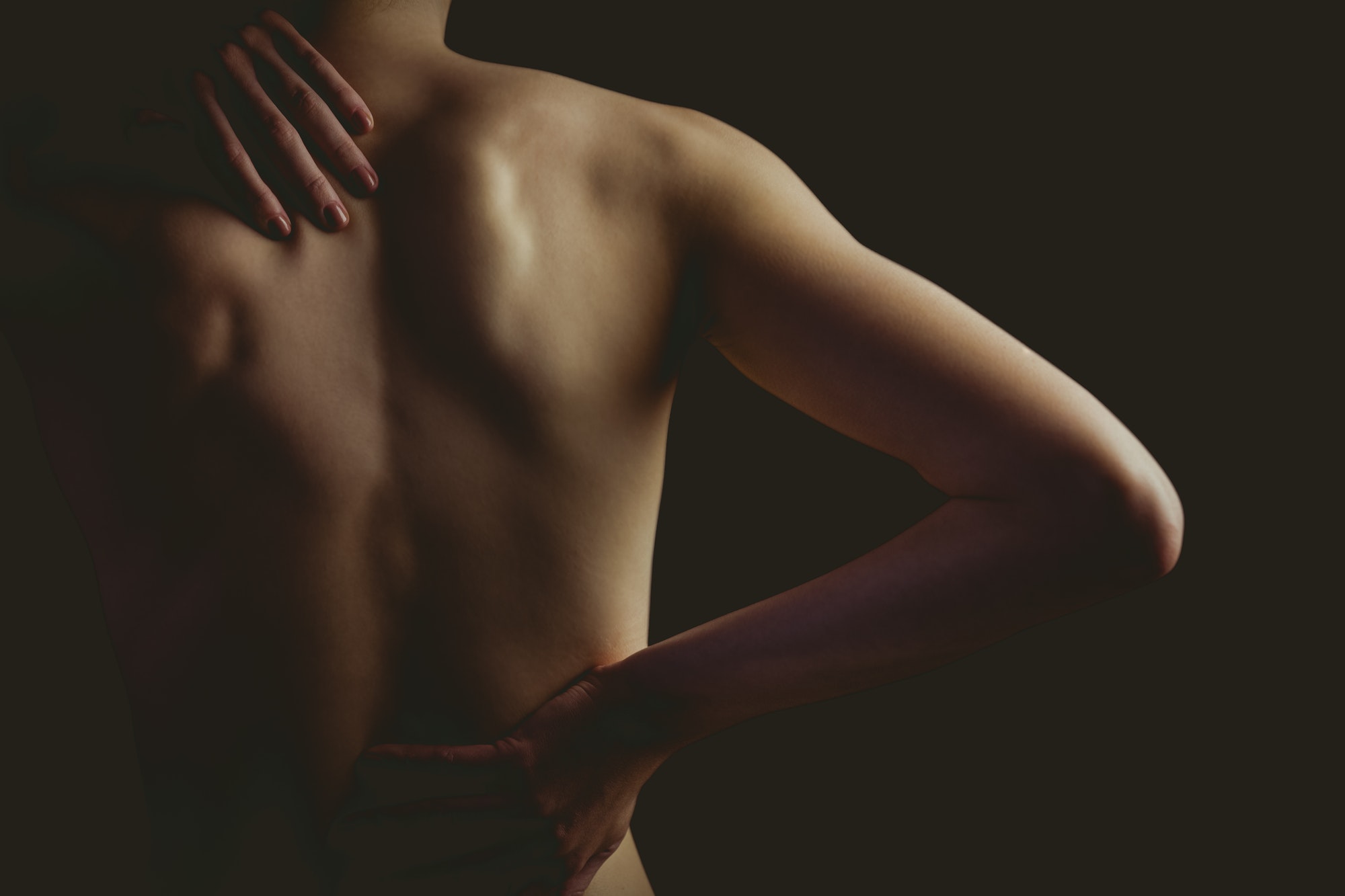 Nude woman with a back injury on black background